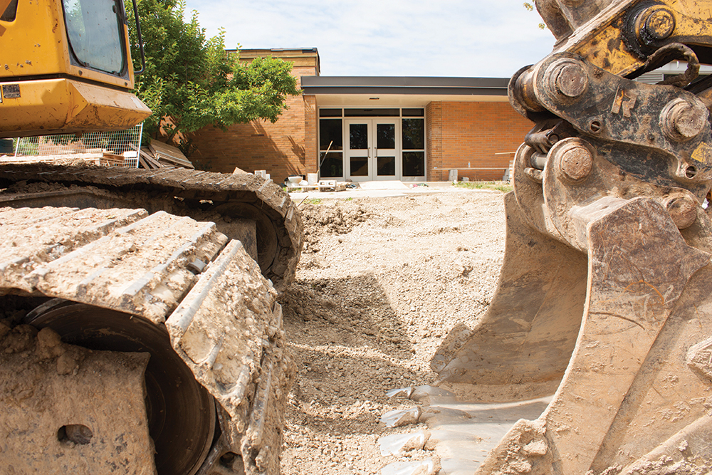 Heavy construction equipment moving dirt at school or government building.